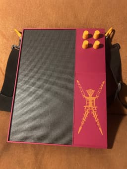Jon's Patternflow powered down, the Burning Man figure inlaid in orange into the front battery panel and the strap clipped to both sides